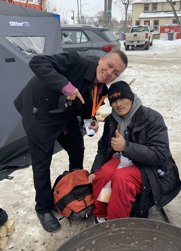 Two men pose for a photo outside a mobile overdose prevention site in the snow.